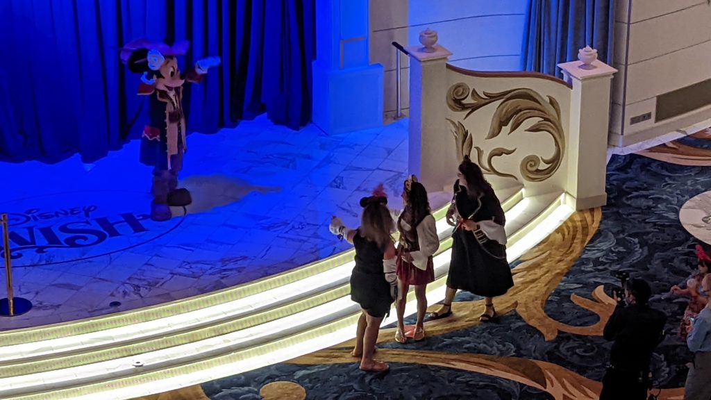 Cruise guests greet Mickey Mouse in the Grand Hall of the Disney Wish, where there's always something going on.